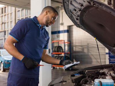 Hyundai mechanic stands in workshop and does an oil check on a car.