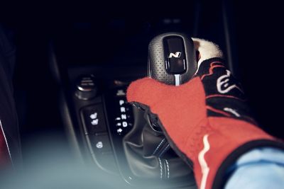 Main gantée d’un pilote de course saisissant le pommeau de levier de vitesses du SUV sportif Hyundai KONA N.