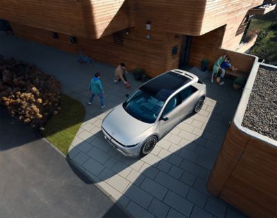 Ein Hyundai IONIQ 5 mit Panorama-Glasdach in der Vogelperspektive parkt vor einem modernen Holzhaus.
