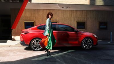 The Hyundai i30 Fastback N Line parked in the city next to a woman.