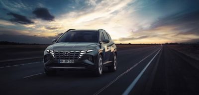 Hyundai TUCSON jedoucí po silnici při západu slunce.