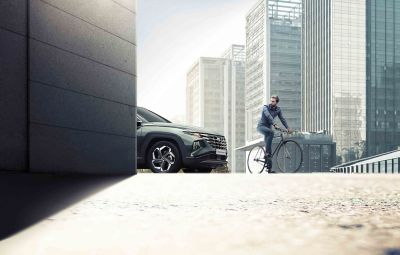 A man cycling in the city in front of the  Hyundai TUCSON Plug-in Hybrid compact SUV.