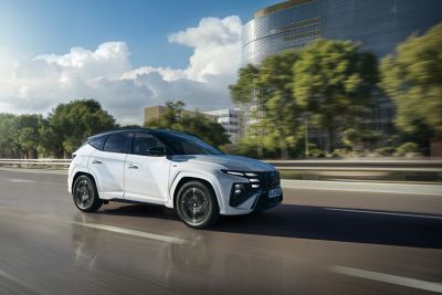 Hyundai TUCSON jazdiaci po mestskej ulici s viditeľnými modernými budovami.