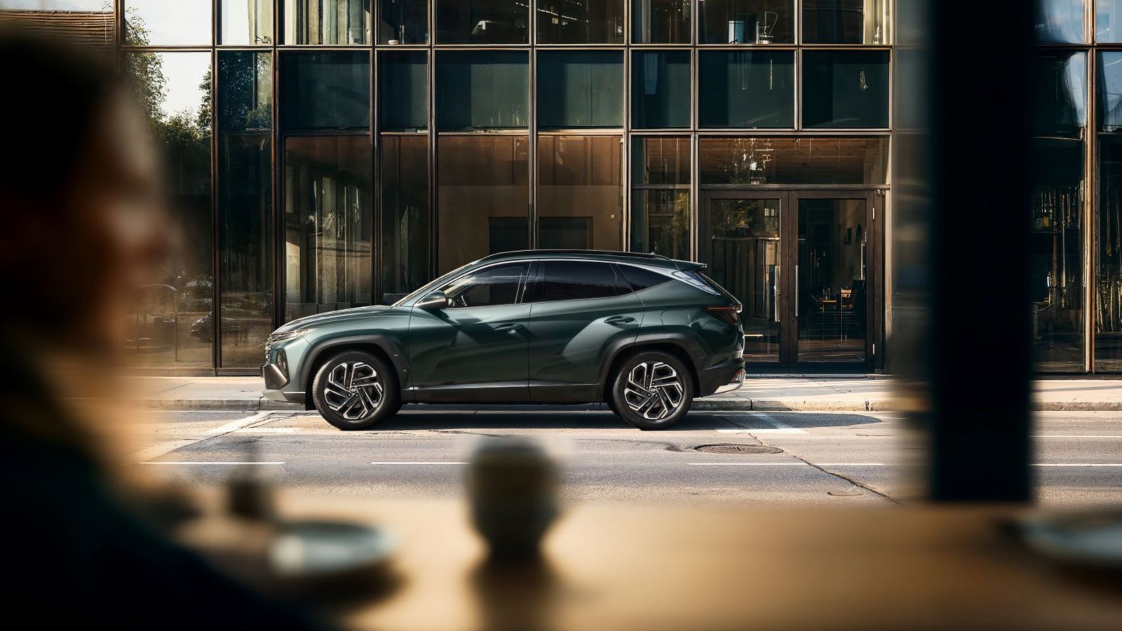 En mörkgrön Hyundai parkerad på en gata framför en modern byggnad.