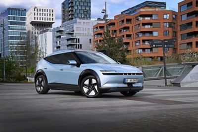 Driekwart vooraanzicht Hyundai IONIQ 3 geparkeerd op dak gebouw met moderne flats op de achtergrond.