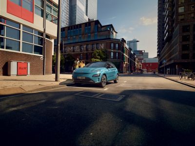 Immagine di Nuova KONA Electric parcheggiata lungo una strada di città con una coppia di ragazzi che le cammina a lato