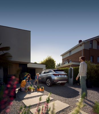 Immagine di Nuova TUCSON Plug-in Hybrid parcheggiata in un giardino di casa con famiglia attorno