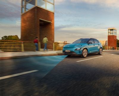 Nový Hyundai Kona Electric s asistenčním systémem pro předcházení kolizi, jedoucí  po mostě.