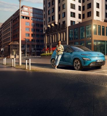 Mujer apoyada sobre el nuevo Hyundai KONA Eléctrico en la ciudad.