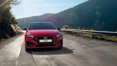 The Hyundai i30 N driving in a hilly set in the colour Engine Red.