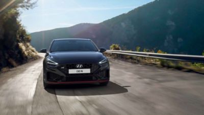 The Hyundai i30 N driving in a hilly set in the colour Phantom Black Pearl.