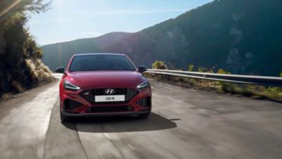 The Hyundai i30 N driving in a hilly set in the colour Sunset Red.