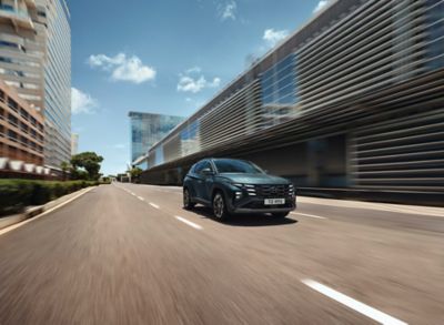 The Hyundai TUCSON Plug-in Hybrid driving down a city street with modern buildings visible.