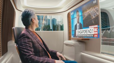 Interior view of a Hyundai future mobility Purpose Built Vehicle with a man watching TV.