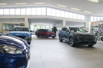 Interno dello showroom con in primo piano cofano di i20 blu, al sinistra KONA blu, al centro KONA rossa e a destra TUCSON Blu