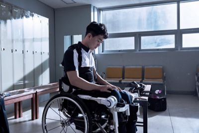En mann i rullestol med skinner på bena. Foto. 
