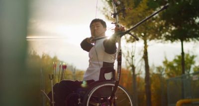 Paraolimpijczyk Jun-beom Park siedzący na wózku inwalidzkim podczas treningu łuczniczego.