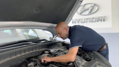 Uomo lavora sul motore di auto con cofano aperto