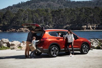 A Hyundai SANTA FE parked next to a lake, a family getting their hiking gear from the opened trunk.