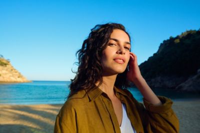 Mujer de pie en una playa tocándose el pelo.