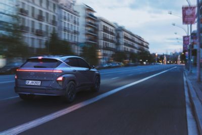 The Hyundai KONA Electric in blue driving down a road. 