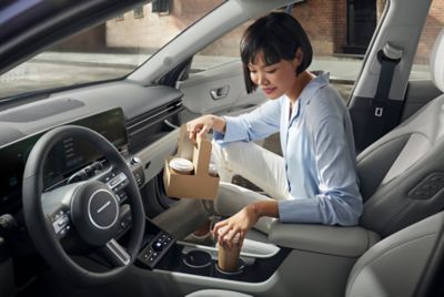 A woman putting her coffee on one of the rotational cup holders of the Hyundai KONA.