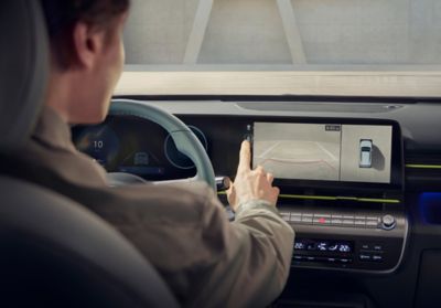 Muž používá dotykovou obrazovku s prostorovým monitorem vozu Hyundai KONA při parkování.