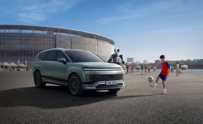 Roboten Atals og en liten gutt soiller fotaball rundt en IONIQ 9. Foto.. Foto.