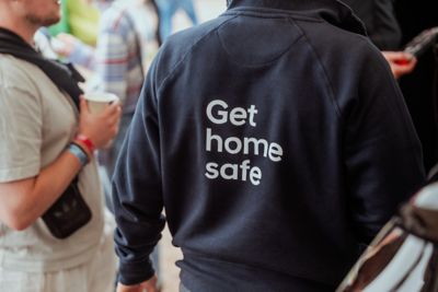 Ryggen til en arrangør med Get Home Safe jakke. Foto.