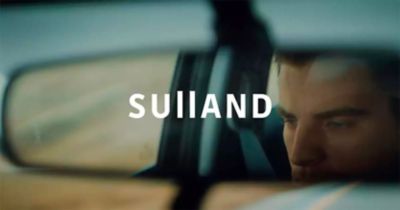 Bilde av en mann som synes i bakspeilet med Logoen SULLAND over bildet. Foto.