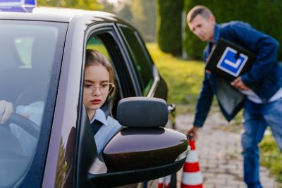 Driving Test. Training parking. Cones for the examination, driving school concept. Alert nervous young teen girl student driver taking driving education lesson test from male instructor.