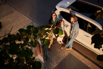 Ein Mann, eine Frau und zwei Mädchen aus der Vogelperspektive, neben einem geparkten Hyundai SANTA FE Plug-in-Hybrid stehend. 
