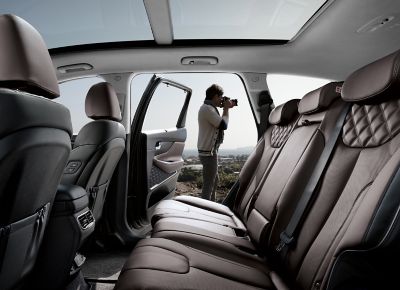 Innenansicht des Hyundai SANTA FE Plug-in-Hybrid mit offener Hintertür, die den Blick auf einen fotografierenden Mann freigibt.