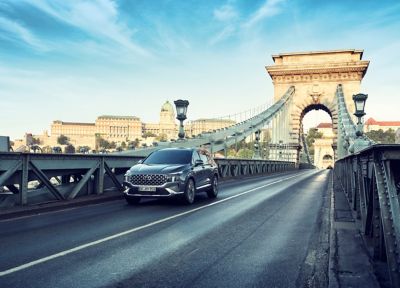 Ein Hyundai SANTA FE fährt über eine historische Brücke vor einer Stadtkulisse mit Schloss.