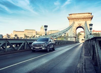 The new Hyundai Santa Fe Hybrid 7 seat SUV in grey driving over a bridge.