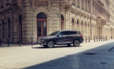 The Hyundai SANTA FE Plug-in Hybrid parked in a city, a man and woman with shopping bags approaching.