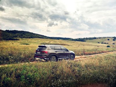 Nový Hyundai Santa Fe Plug-in Hybrid, 7 sedadlové SUV, který jede po venkovské silnici v kopcích.