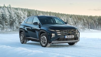Mörk TUCSON Hybrid som kör på snöing landsväg vintertid.