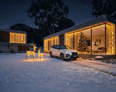TUCSON Hybrid N Line garé dans une allée enneigée devant une maison moderne illuminée pour noël