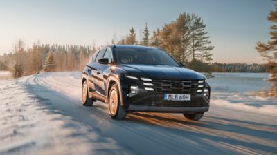 Hyundai TUCSON Plug-in Hybrid på en snötäckt väg i vinterlandskap.