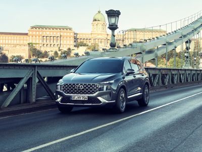 Nowy 7-miejscowy SUV Hyundai SANTA FE Plug-in Hybrid jadący przez miasto – ujęcie z tyłu.