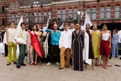 Groepsfoto van modellen, vrouwen en mannen, in kleding van modemerk MARTAN met op de achtergrond een Amsterdams gebouw.