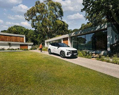 Hyundai TUCSON Hybrid N Line blanc garé dans une allée devant une maison moderne
