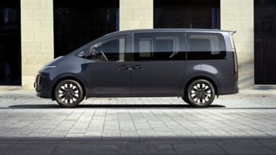 The Hyundai STARIA Hybrid seen from the side in front of a futuristic building.