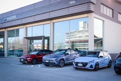 Esterno dello showroom, con parcheggiate da destra a sinistra di tre quart da davanti i20N azzurra, KONA Hybrid azzurra, KONA rossa