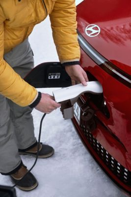 Mann bruker V2L lader på en KONA Electric. Foto.