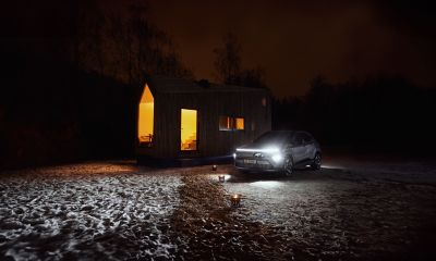 Vju kompakthytte med en KONA Electric parkert utenfor i mørket som gir lys til hytta. Foto.