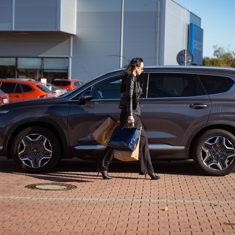 Šedý Hyundai SANTA FE Hybrid zaparkovaný na ceste pod stromami s jesenne sfarbeným lístím