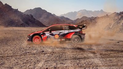 Een Hyundai i20 N WRC-rallyauto die driftend cirkels maakt in de woestijn.