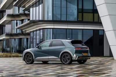 Driekwart achteraanzicht geparkeerde Hyundai IONIQ 5 voor een modern gebouw met veel glas.
